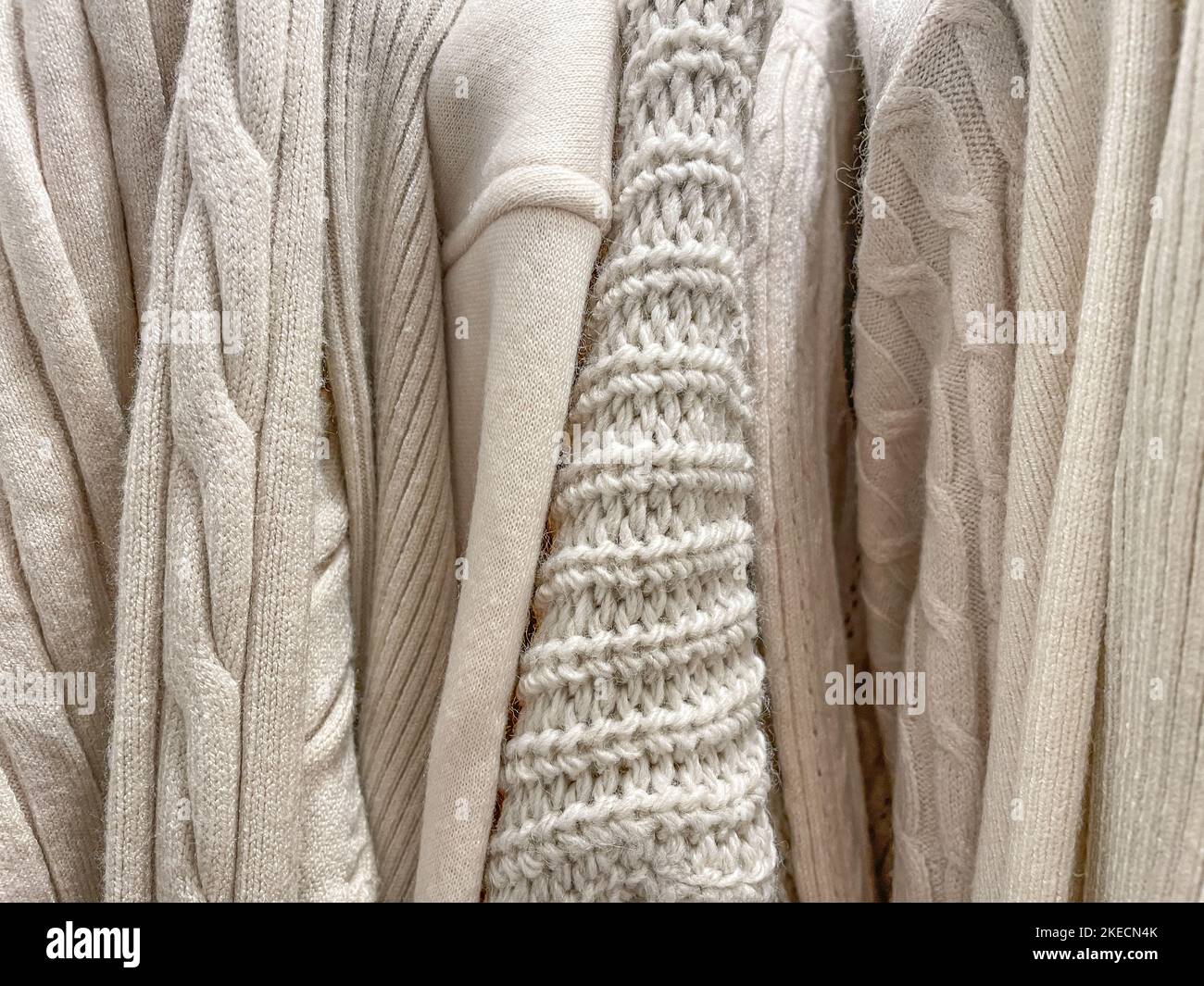 Texture cozy background photo of different knitted sweaters and jumpers of beige cream color hanging in stack in a store. Fall Winter warm clothes col Stock Photo