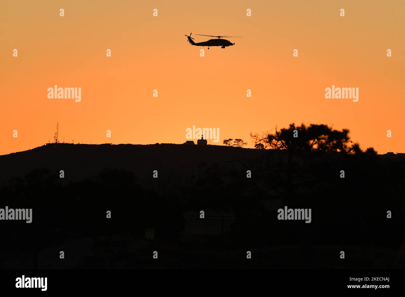 United States Navy MH-60 helicopter flies near Cabrillo National Monument in San Diego, California at sunset, as seen from Coronado, California Stock Photo