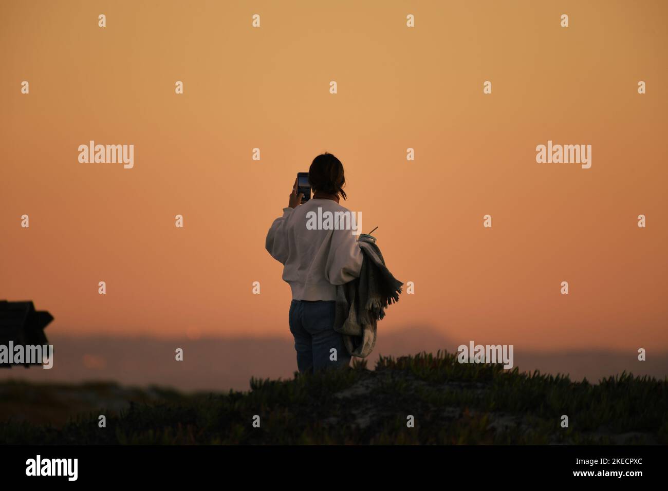 Girl standing on a sand dune, taking a photo of the beach at sunset in Coronado, California Stock Photo