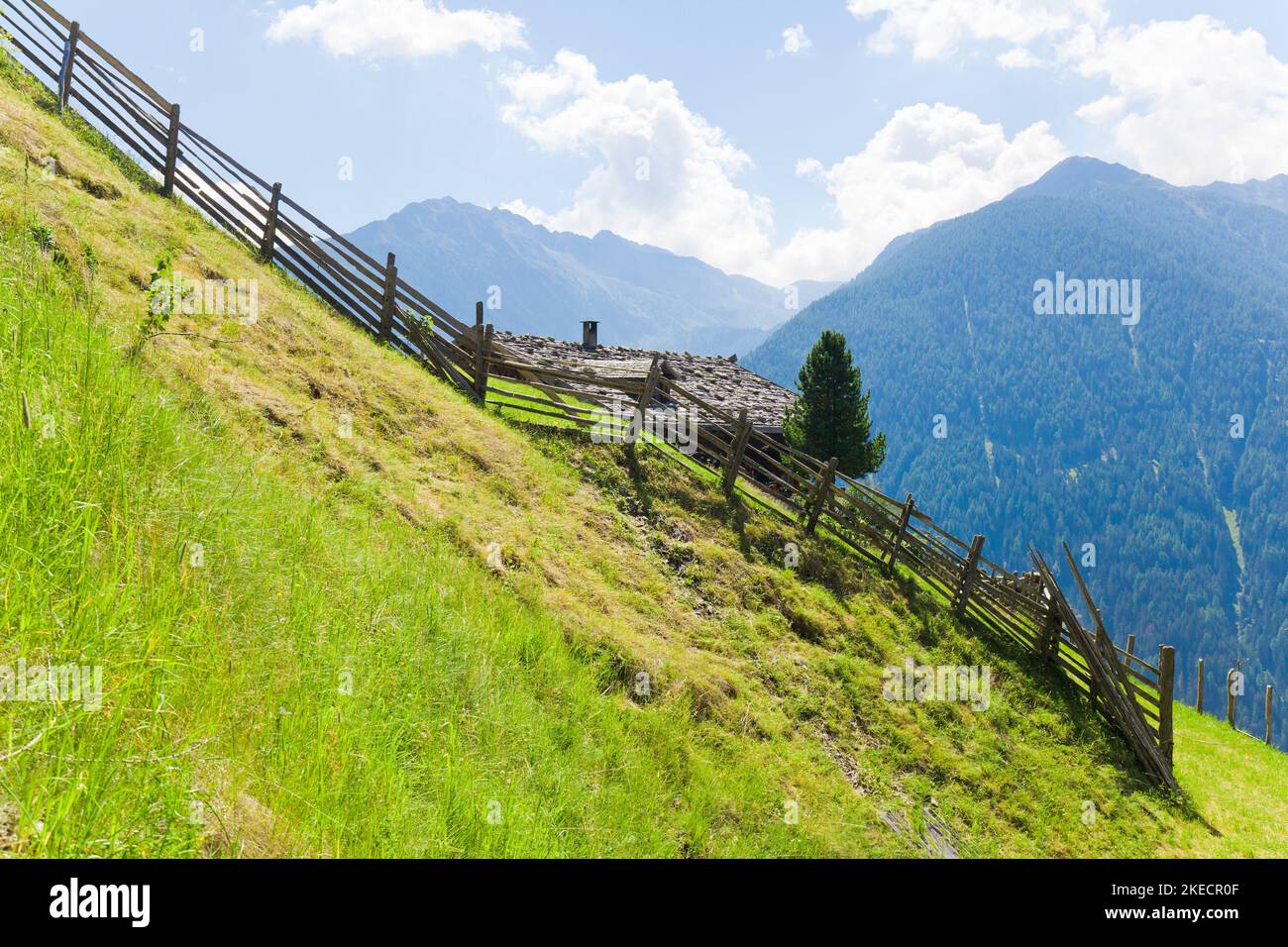 Wooden fence on steep mountain meadow in front of shingle roof of mountain farm in South Tyrol Ulten Valley Stock Photo