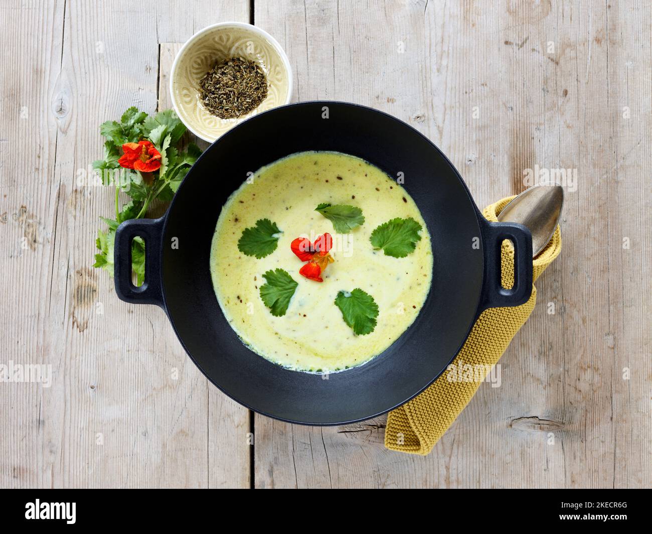 ayurvedic cuisine, buttermilk soup in a black cast iron cooking pot from above, next to a small bowl with cumin, on light rustic wooden table top Stock Photo
