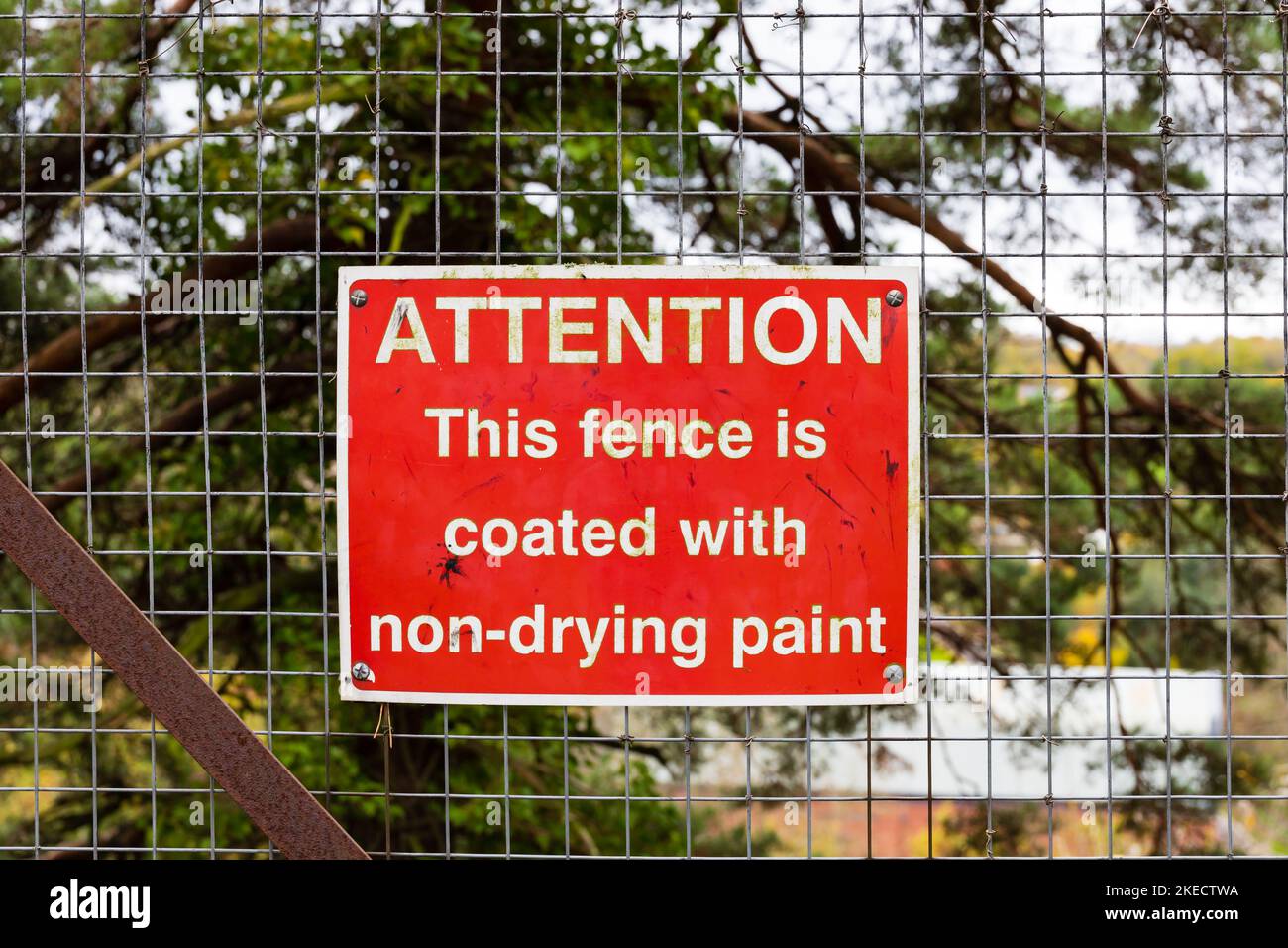 Warning sign. Attention. This fence is coated with non-drying paint. Red sign on mesh fence. Bridgnorth, Shropshire, England. Stock Photo