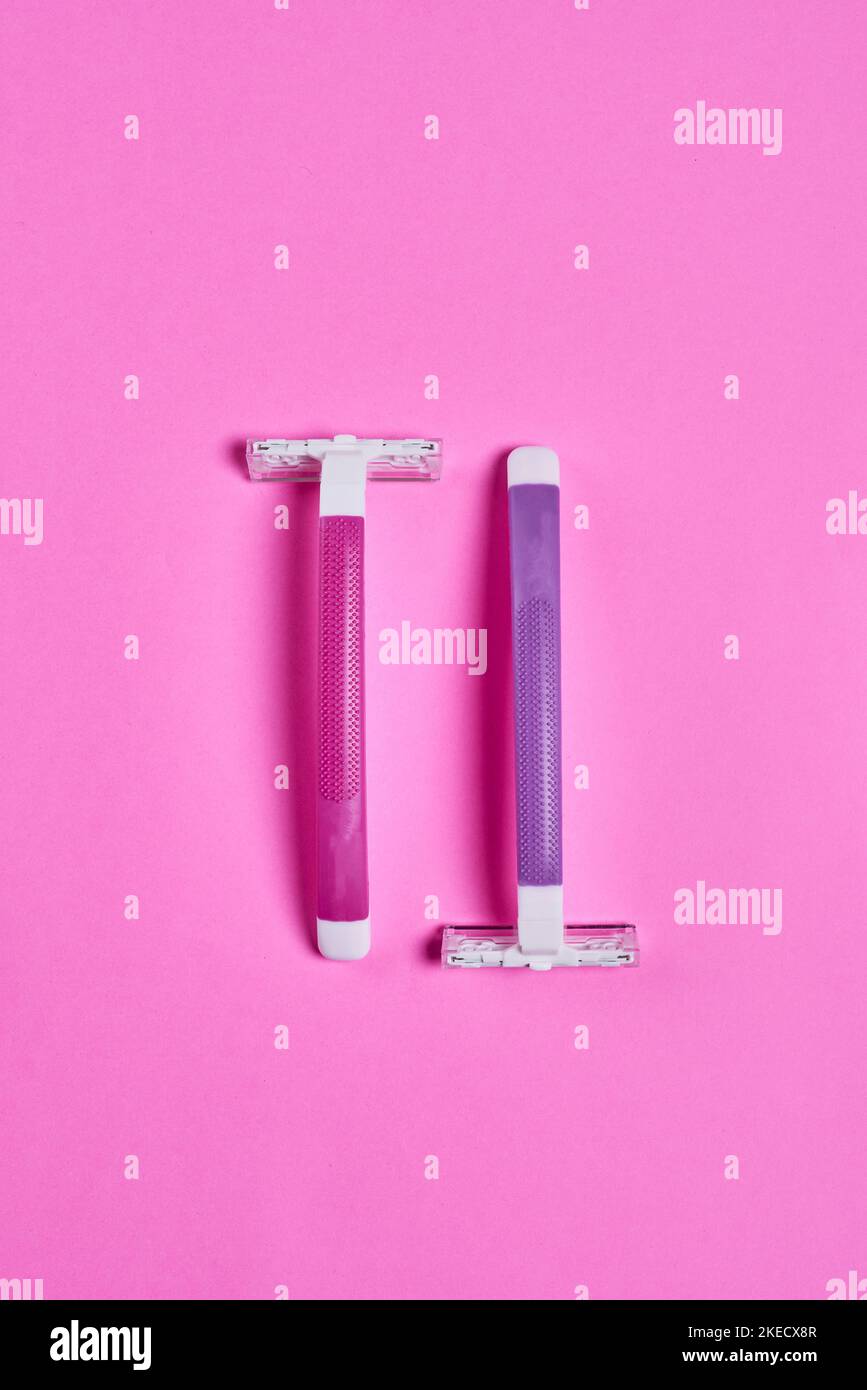 two toothbrushs on a pink background, one is white and the other is blue with a purple handle Stock Photo