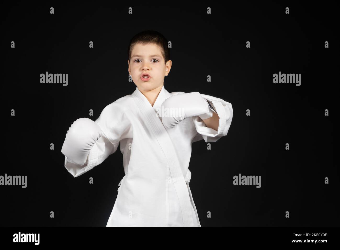 A little boy learns martial arts, doing karate in kimono and boxing gloves hand pads. Stock Photo