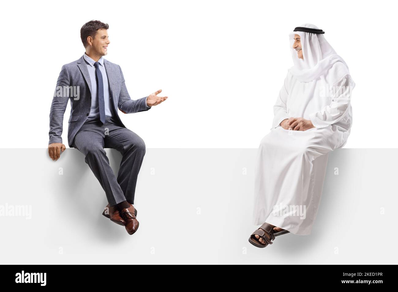Arab man in an ethnic robe sitting on a blank panel and listening to a businessman talking isolated on white background Stock Photo