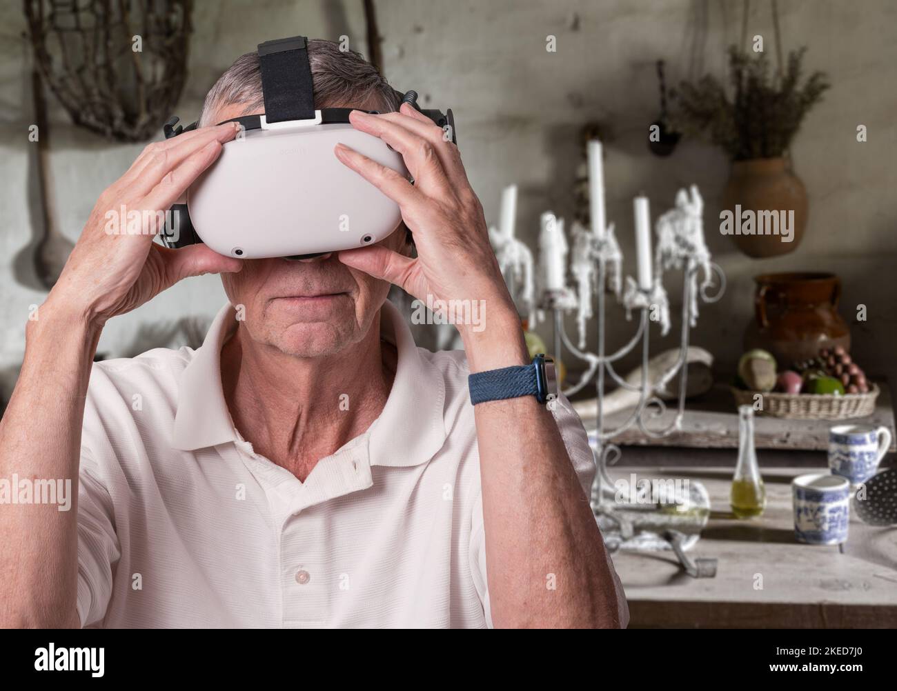 Senior adult man holding his virtual reality headset while exploring a medieval room in the metaverse Stock Photo