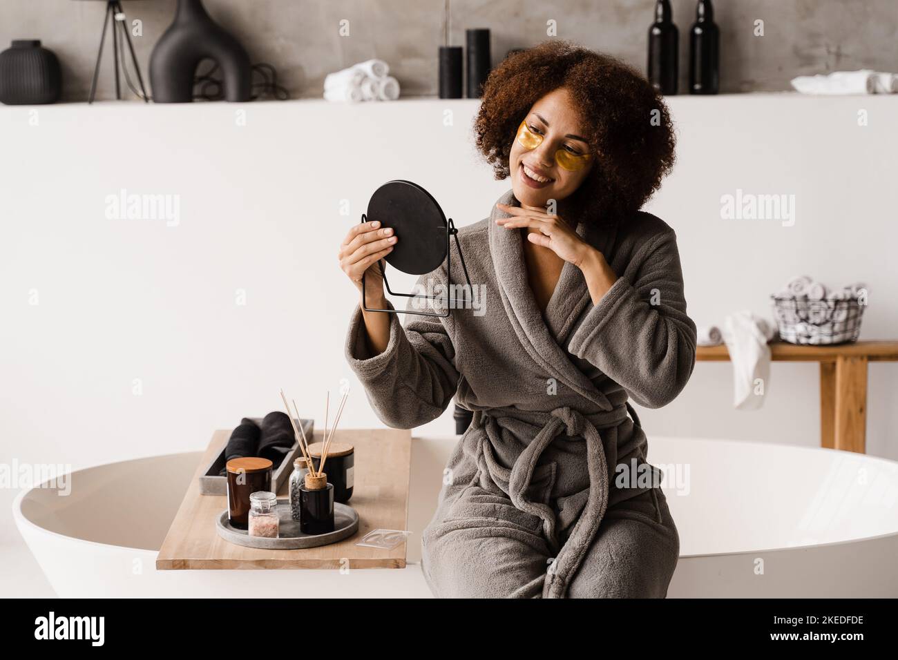 African american woman with golden patches on eyes looks in the mirror ...