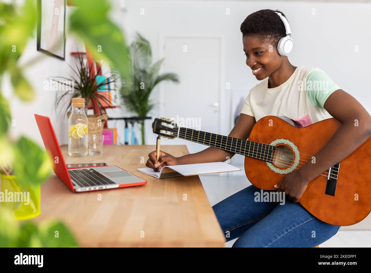 Happy young african woman watching online course learning to play the guitar Stock Photo