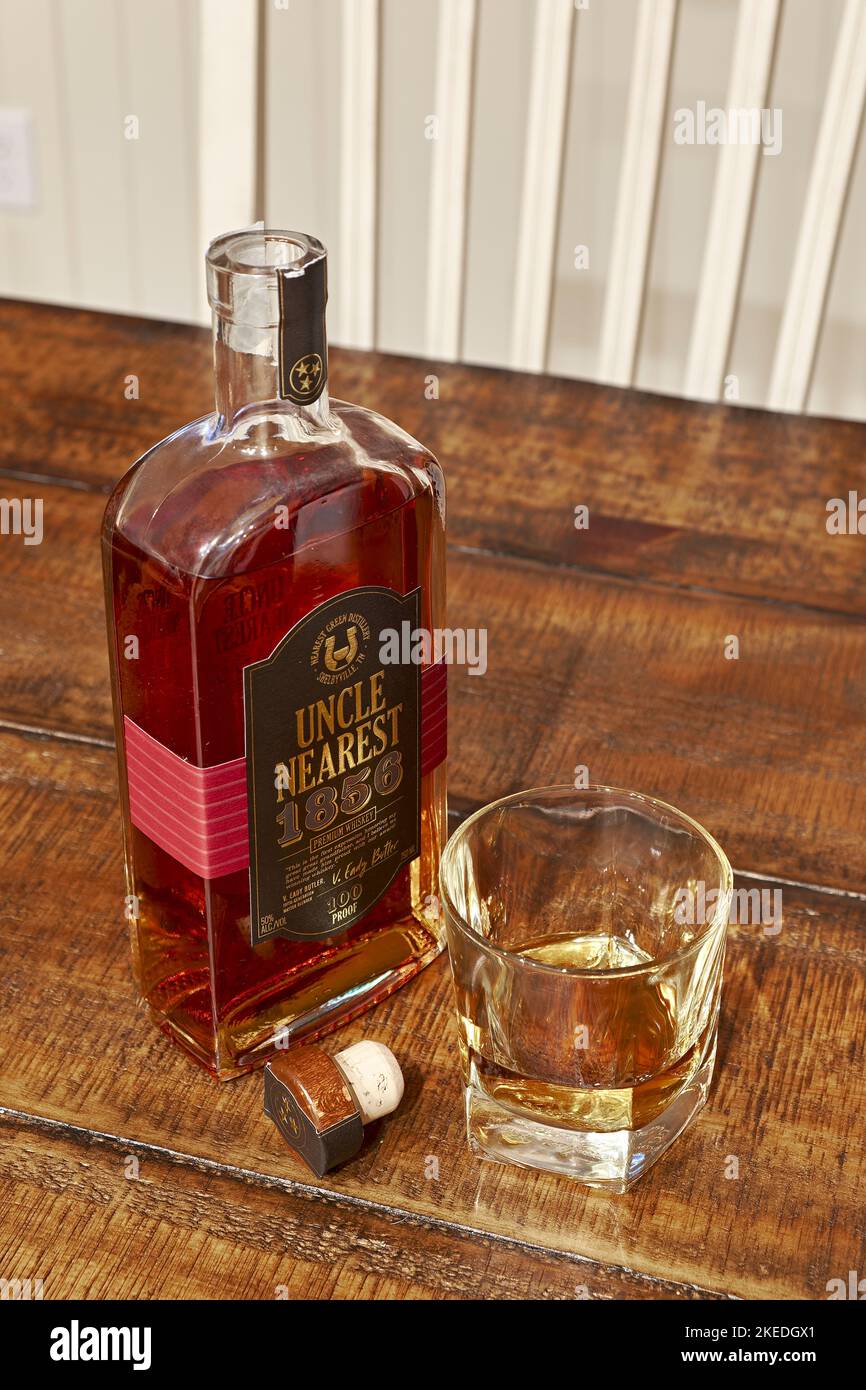 Uncle Nearest, top shelf Tennessee bourbon whisky bottle next to a glass of bourbon, neat, or without ice on a table. Stock Photo