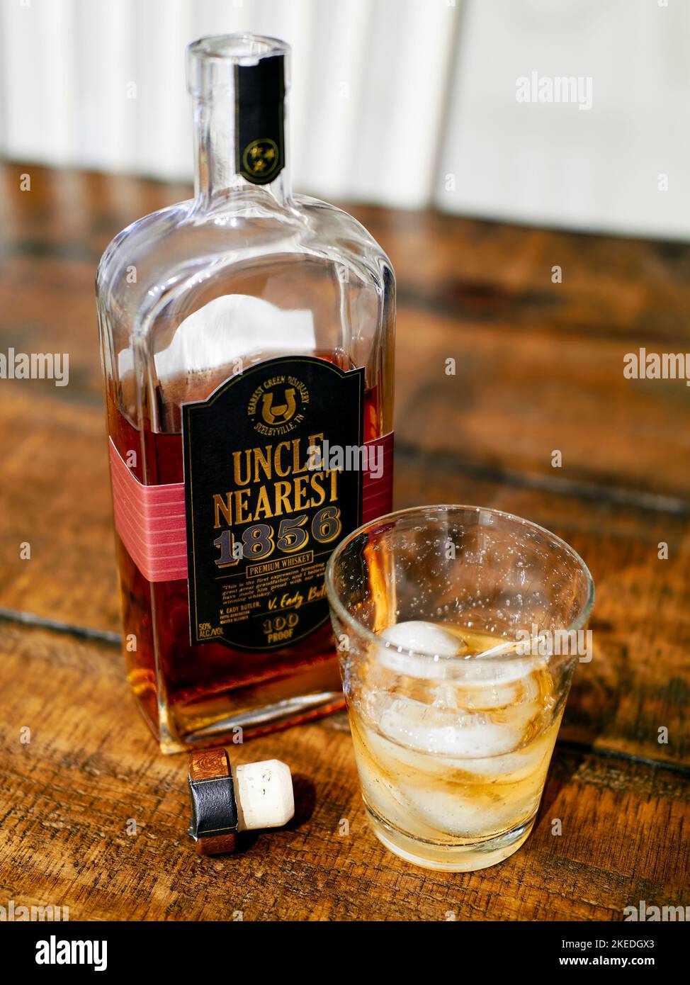 Uncle Nearest, top shelf Tennessee bourbon whisky bottle next to a glass of bourbon,on ice on a table. Stock Photo