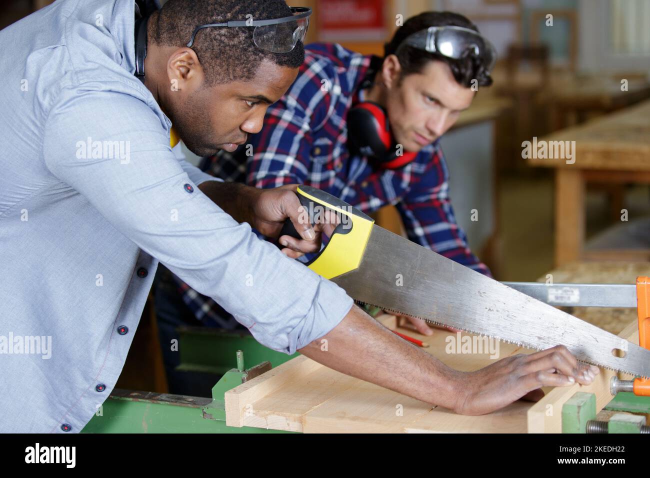 two men in carpentry workshop one using handsaw Stock Photo