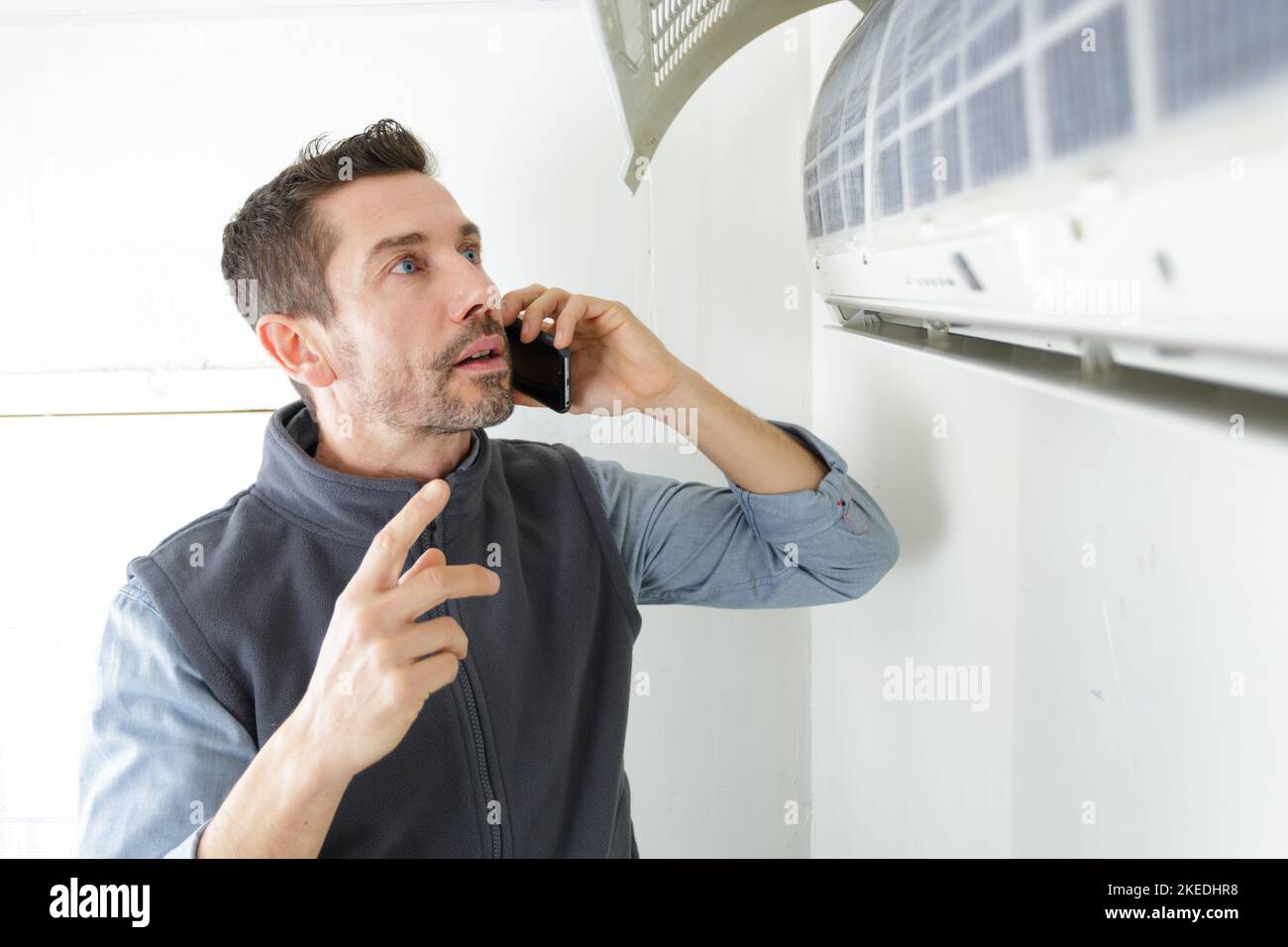 repairman contractor using the phone while repairing heating panel Stock Photo