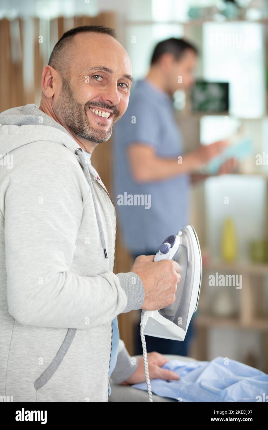man ironing shirt on ironing board with steaming blue iron Stock Photo