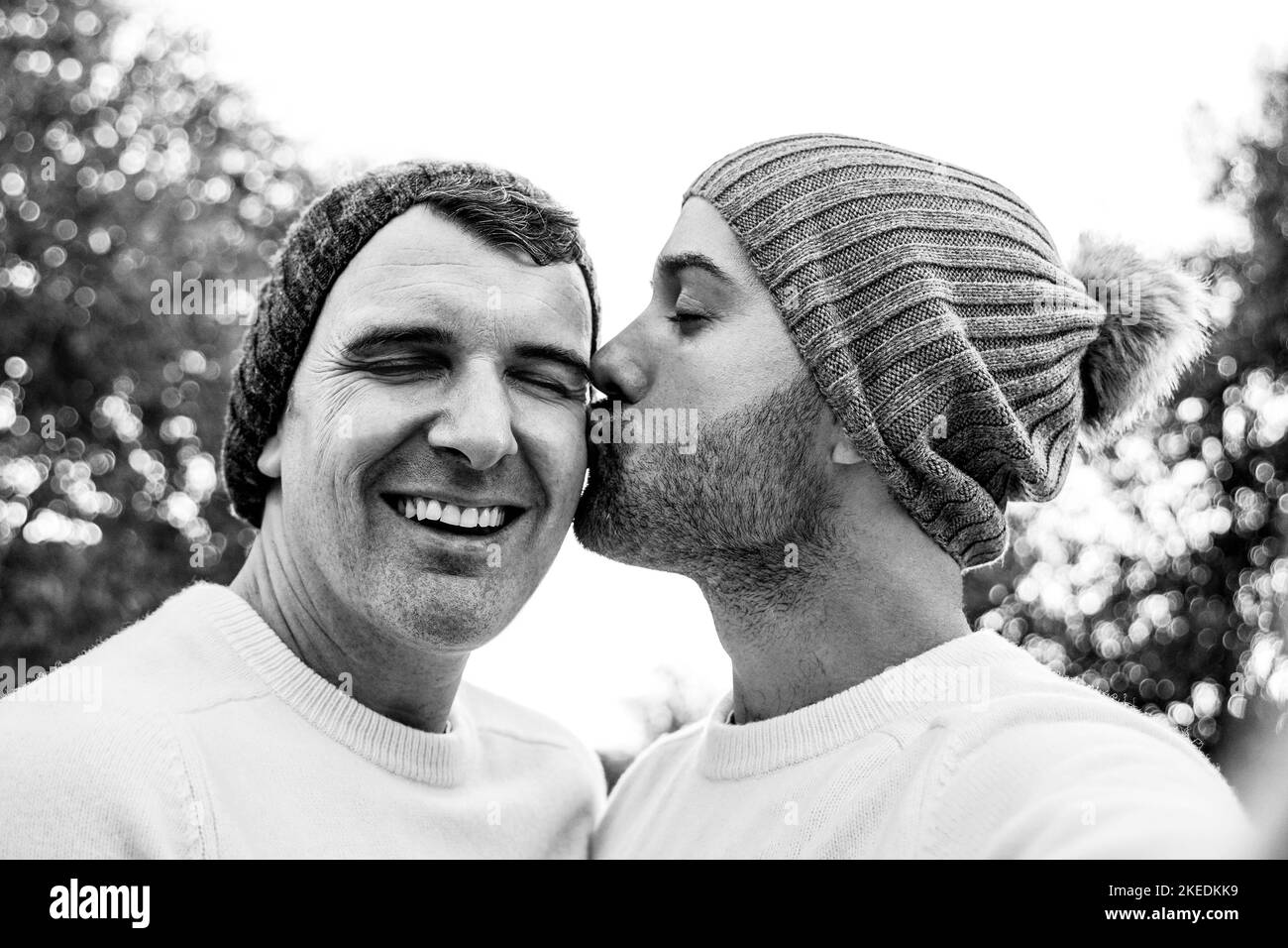 Happy mature gay men couple taking selfie kissing in winter time outdoor - Lgbtq love concept - Black and white editing Stock Photo