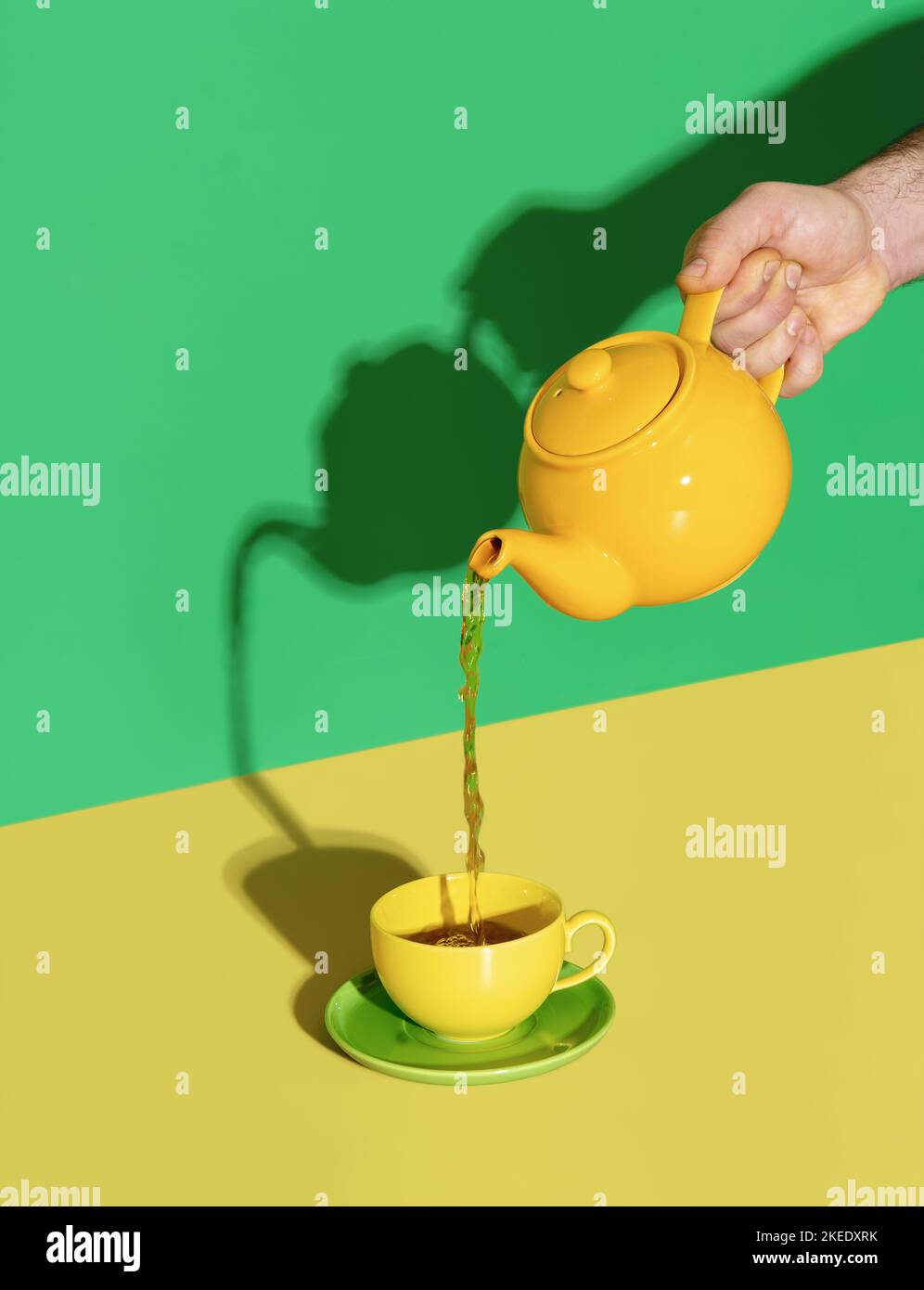 Pouring hot mint tea in a cup, in bright light on a yellow colored table. Pouring tea from a yellow teapot. Stock Photo