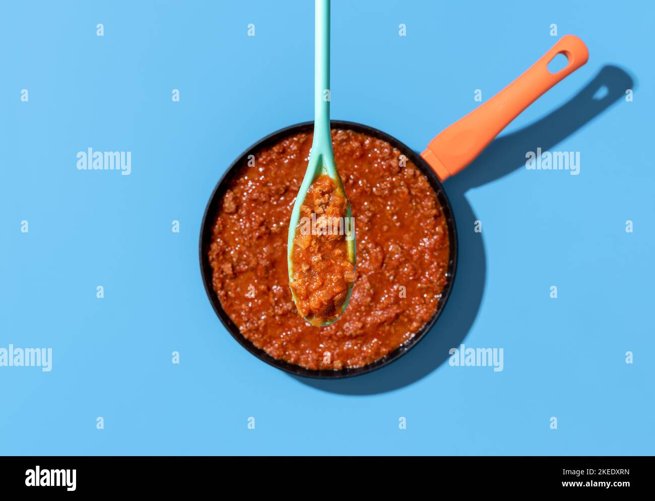Above view with homemade bolognese sauce in a spoon minimalist on a blue table. Classic italian bolognese sauce stewed in a iron cast pot Stock Photo