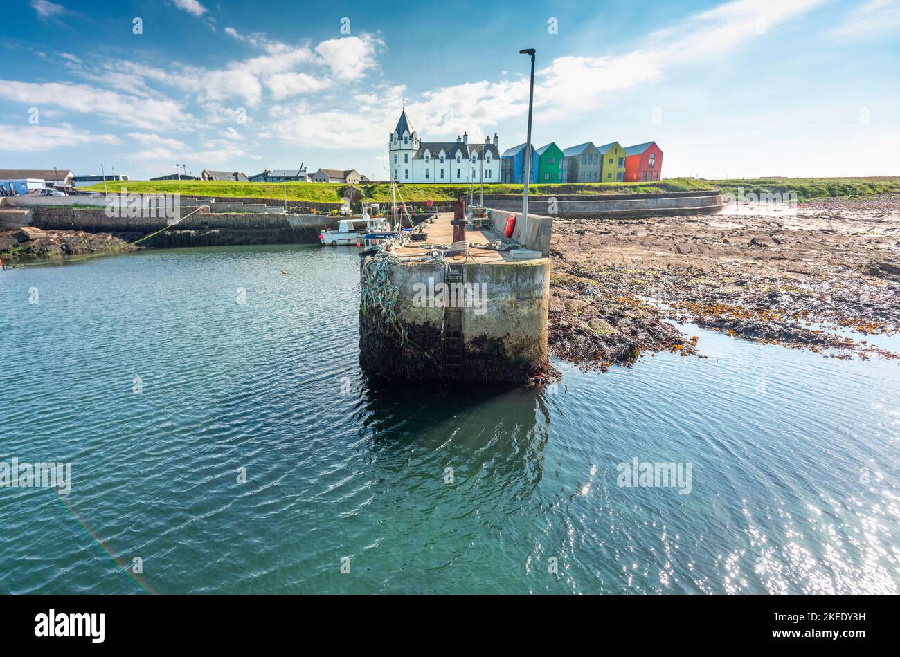The passenger ferry jetty,where people board service to Orkney Islands,calm blue sea,close to iconic tourist landmark with white signpost,hotel and co Stock Photo