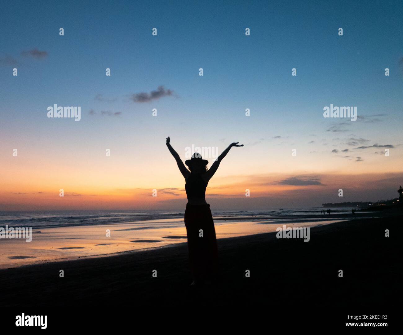 A silhouette of a young woman on the beach enjoying the vibrant sunset ...