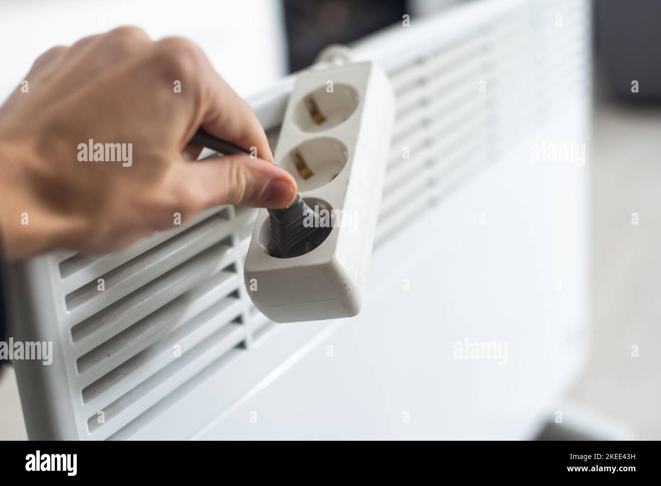 Electric heater plug inserted into extension cord. White radiator for