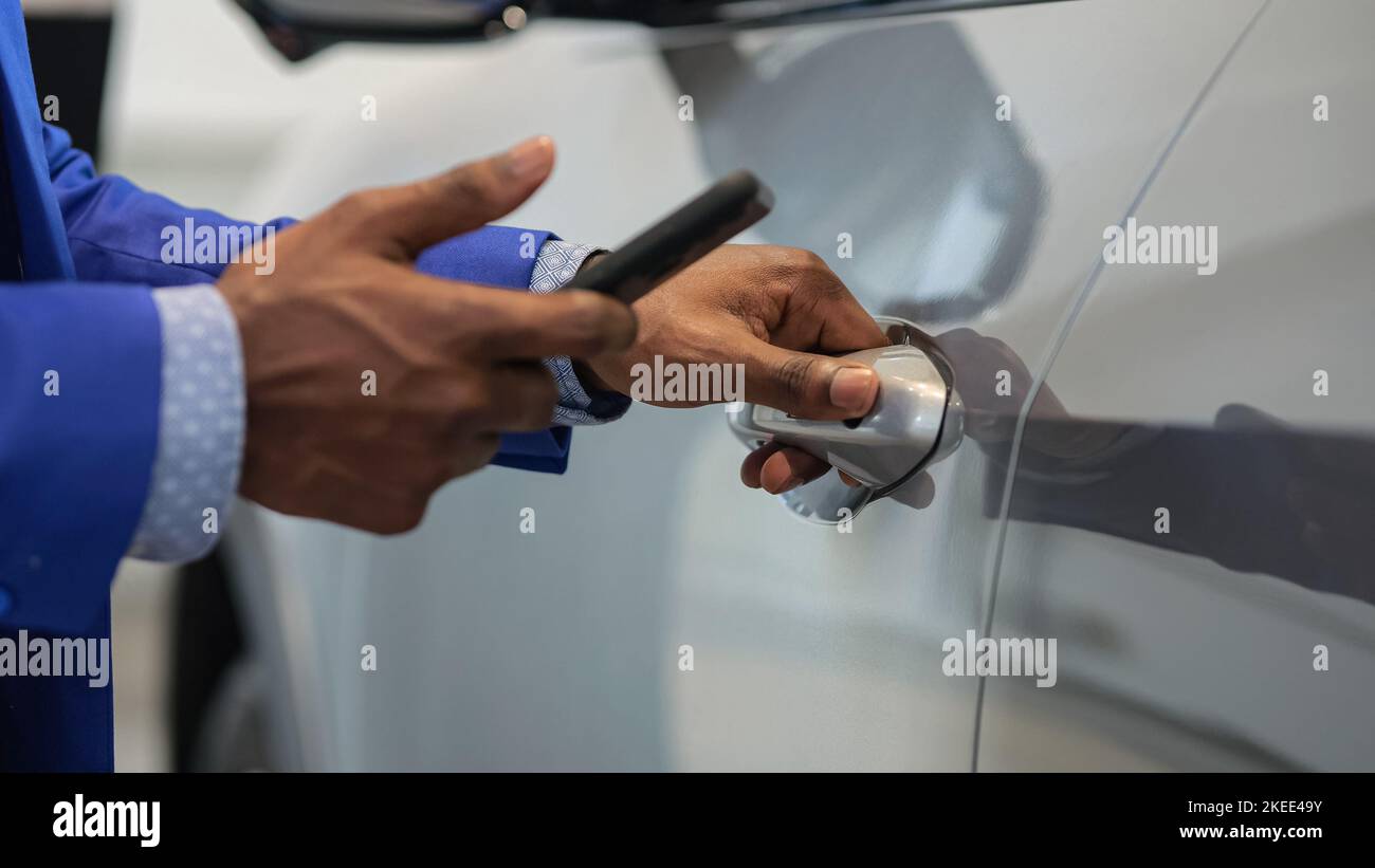 Black salesman opens car using app on mobile phone Stock Photo