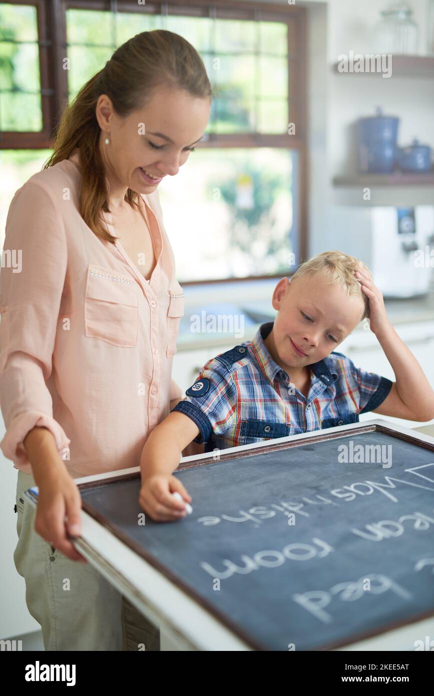 Lets see what needs to be done today. a mother and son writing chores on a chalkboard. Stock Photo