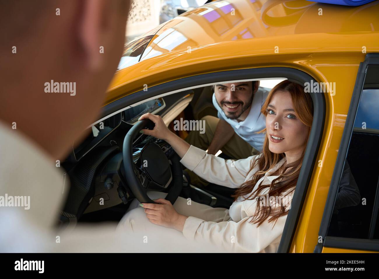 Auto dealership clients seated in vehicle communicating with salesclerk