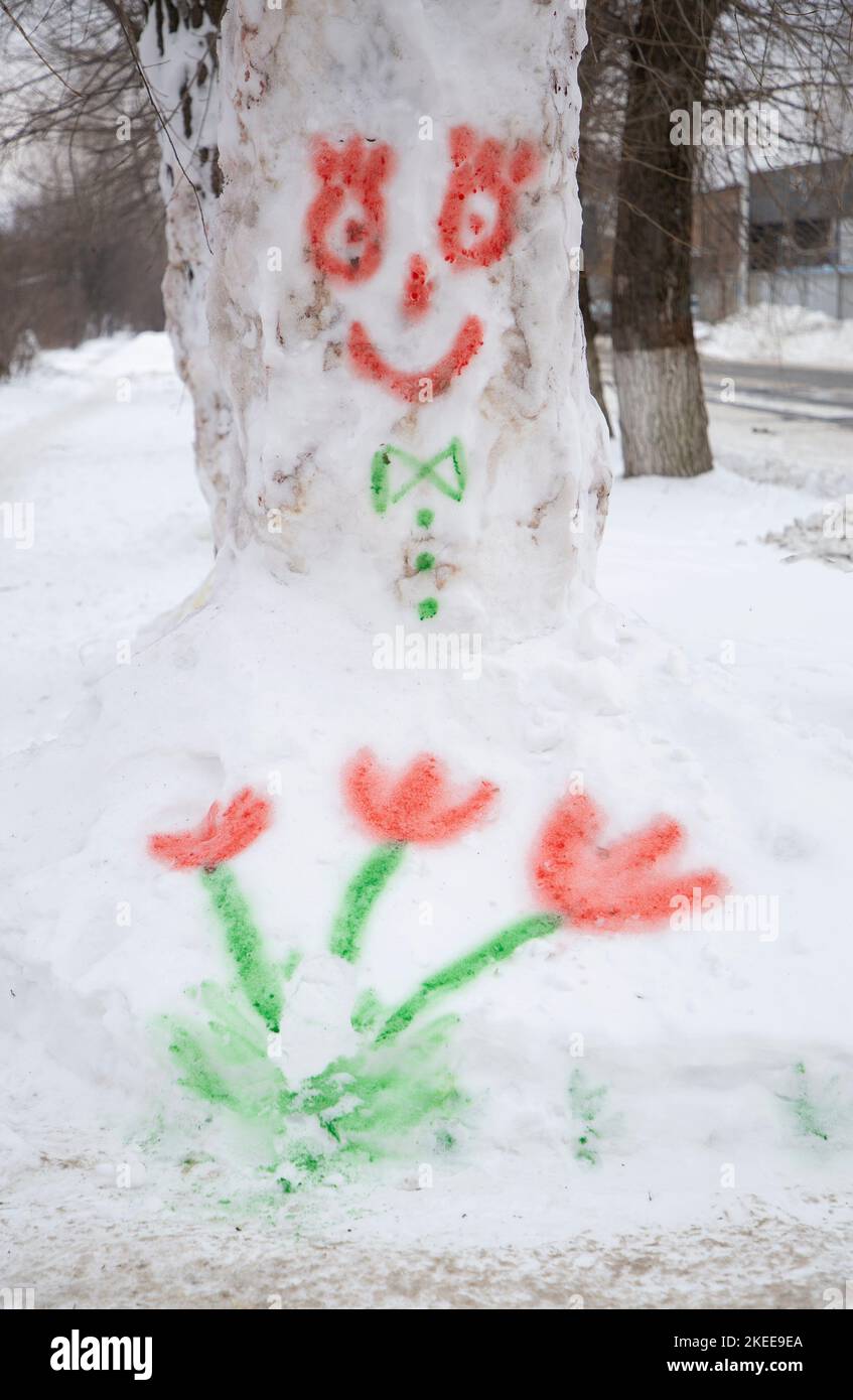 Children's drawing with multi-colored paints on the snow, painted flowers and a funny face. Goodbye winter, hello spring. Educational winter games. Fu Stock Photo