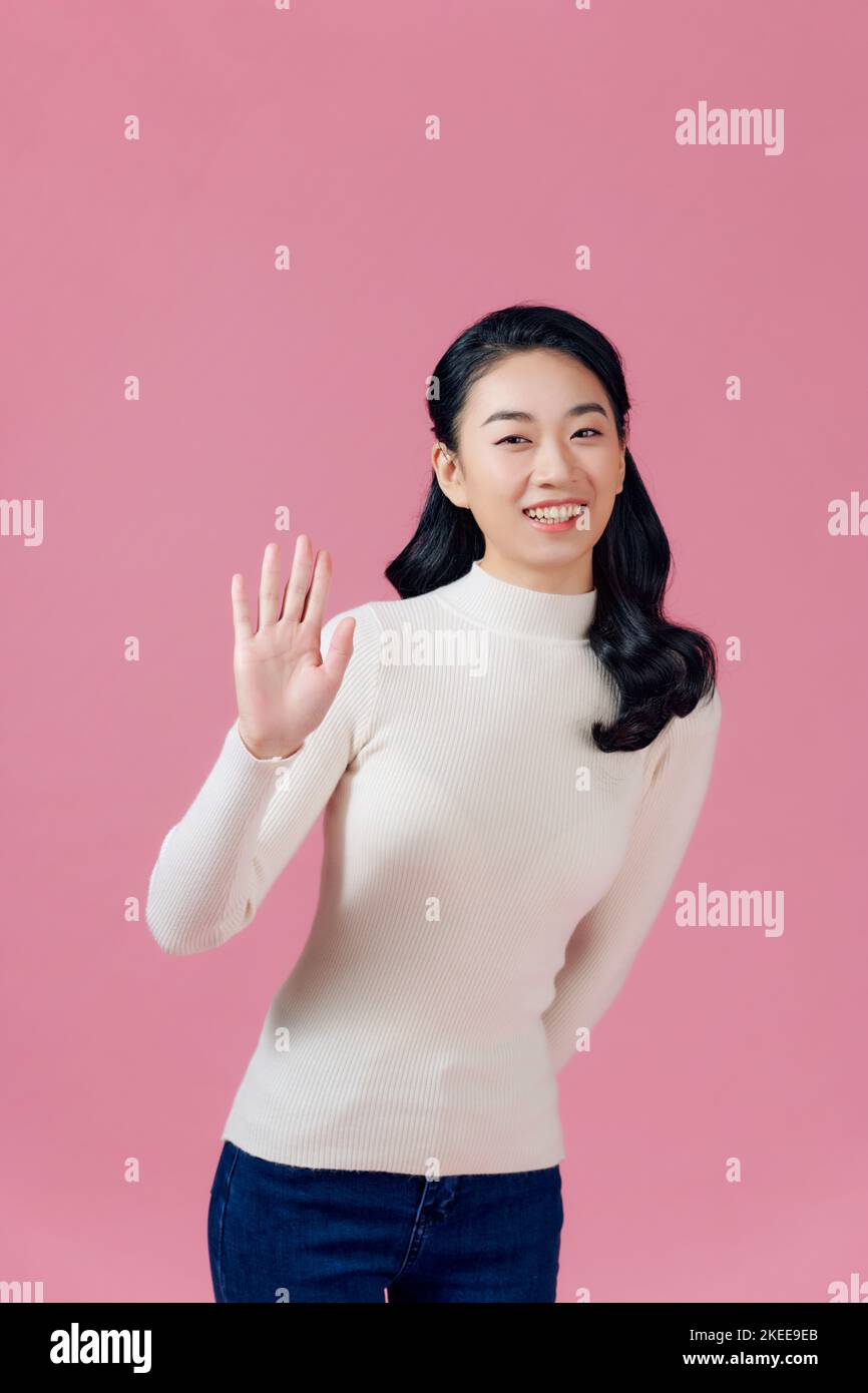 Friendly, pleasant and cheerful east-asian woman raising palm, wave hand greeting and smiling on pink background Stock Photo