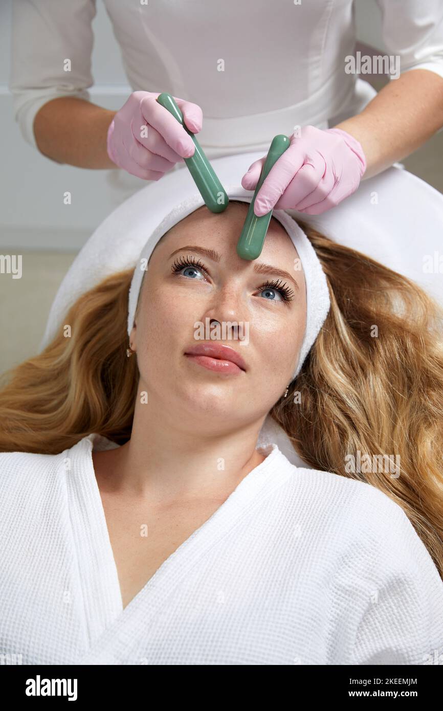 Young woman receiving facial massage with stone sticks in beauty salon