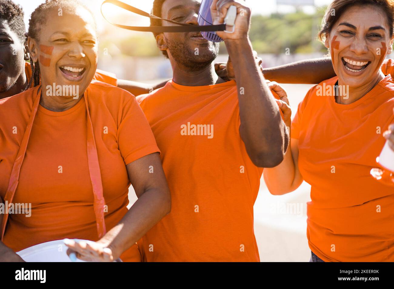 Orange sport fans screaming while supporting their team - Football supporters having fun at competition event - Focus on left african man eye Stock Photo