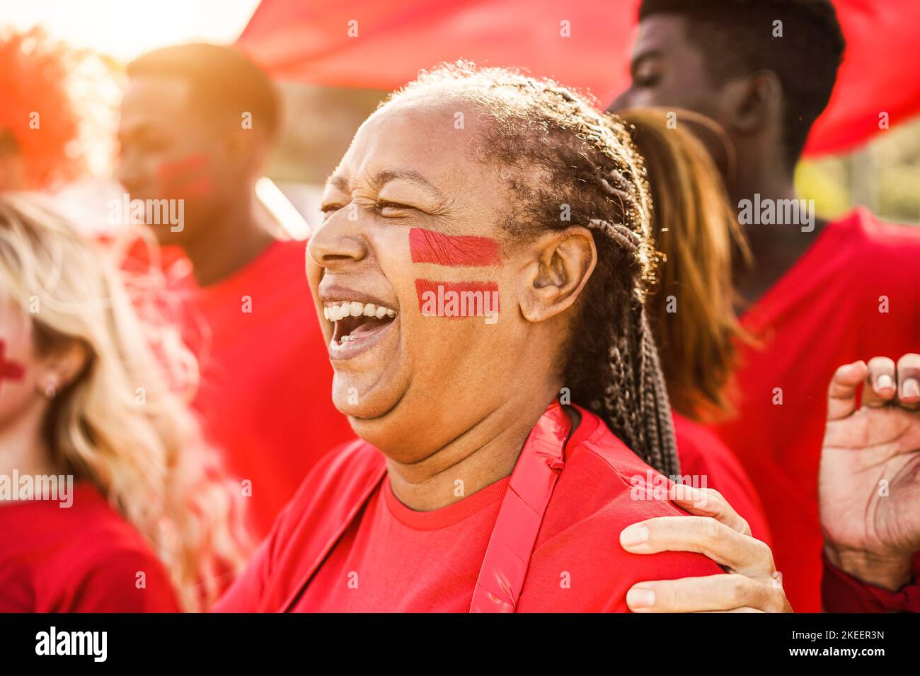 African red sport fans screaming while supporting their team - Football supporters having fun at competition event - Focus on senior woman face Stock Photo