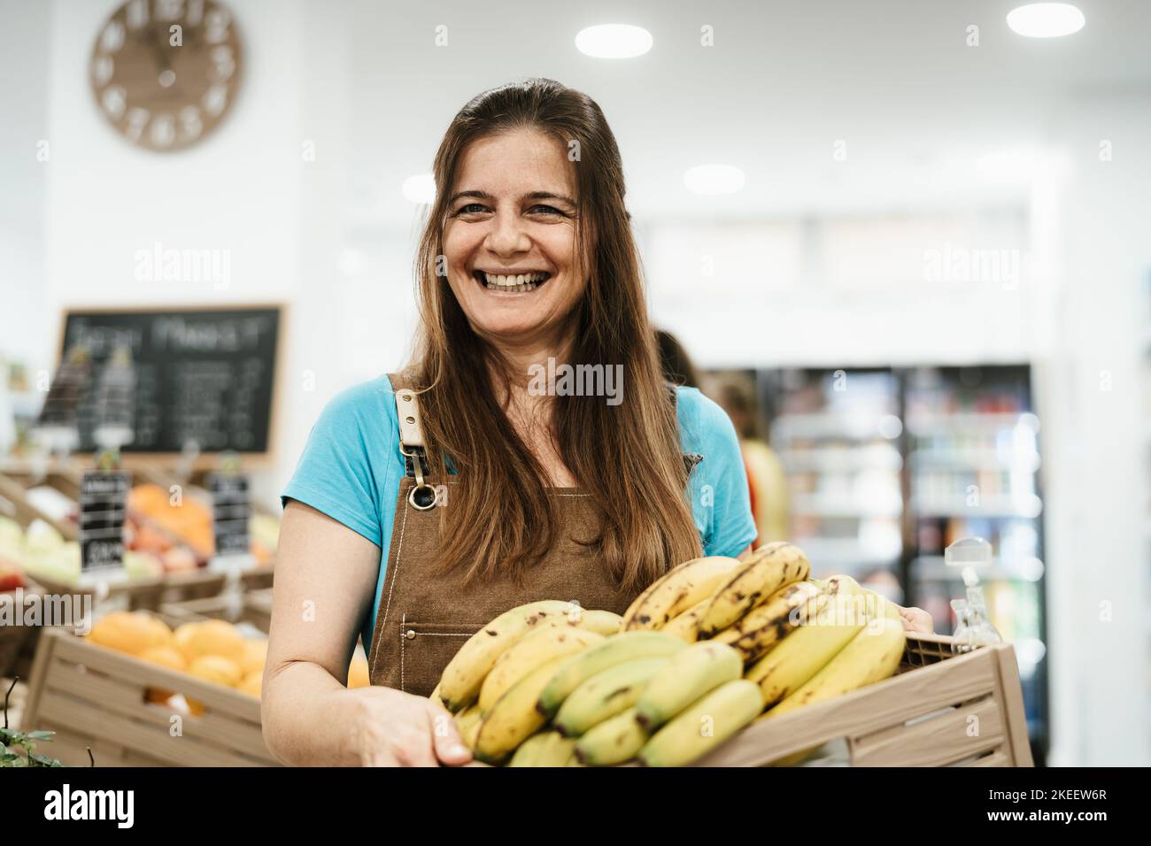 Happy woman working inside supermarket holding a box containing fresh bananas Stock Photo