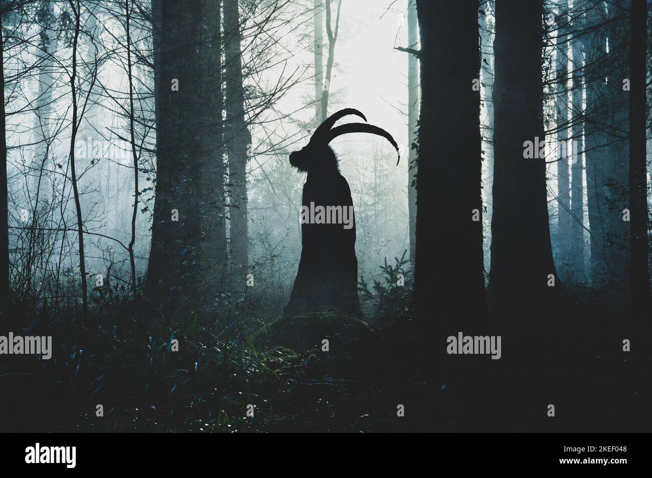 A fantasy concept of a pagan horned goat like figure. Silhouetted against the light. In a spooky forest in winter. With a textured edit. Stock Photo