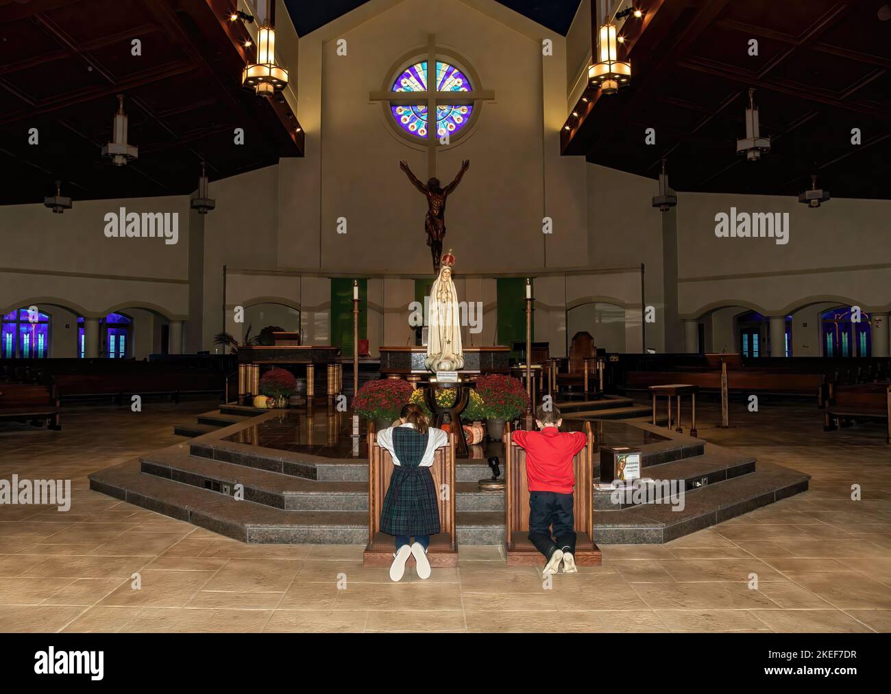 Two St. Ambrose Catholic School students kneeling in veneration before the traveling statue of Our Lady of Fatima at St. Ambrose Catholic Church. Stock Photo