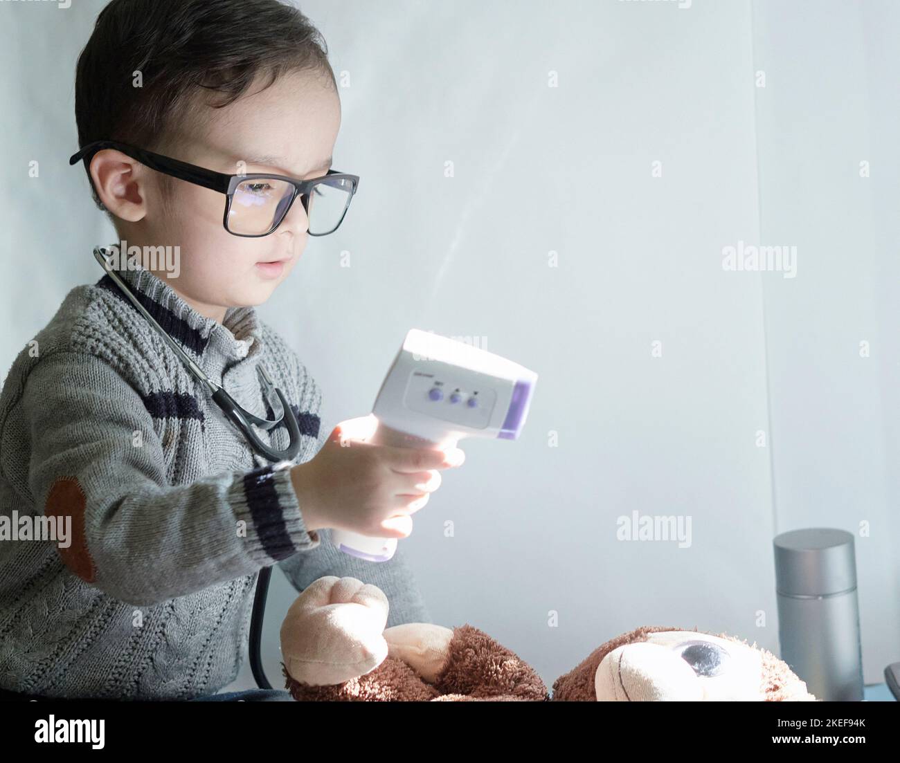 a young boy playing with a remote control device and stuffed animals on a table in front of the tv screen Stock Photo