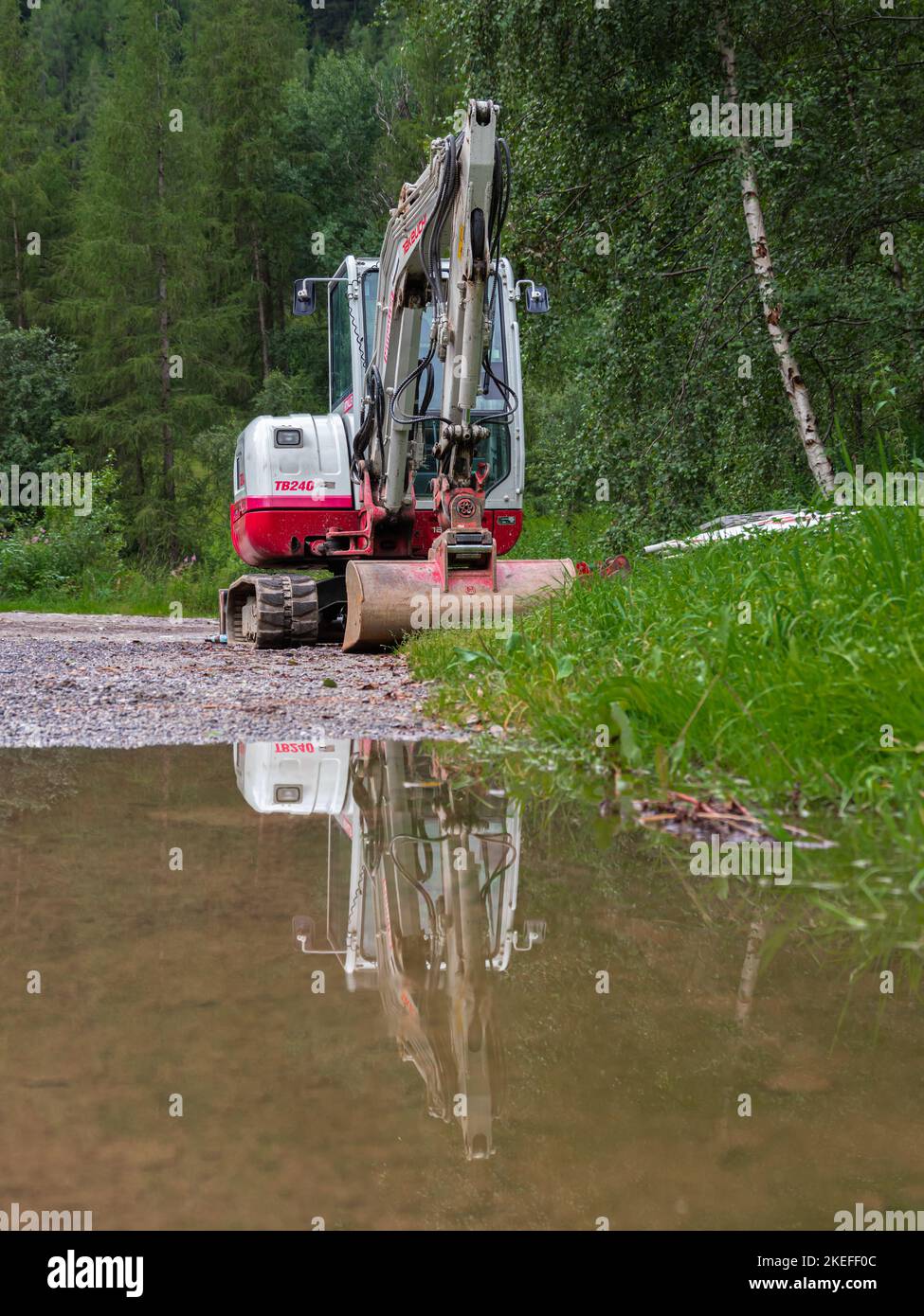 Umhausen, Austria - July 26, 2022: A working machine - a digger - and its reflection in a rain puddle Stock Photo