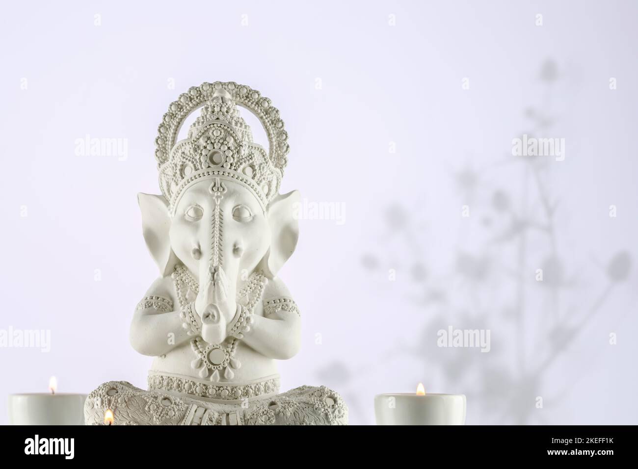 Sculpture of Lord Ganesha with candles on a gradient light background with shadows and copy