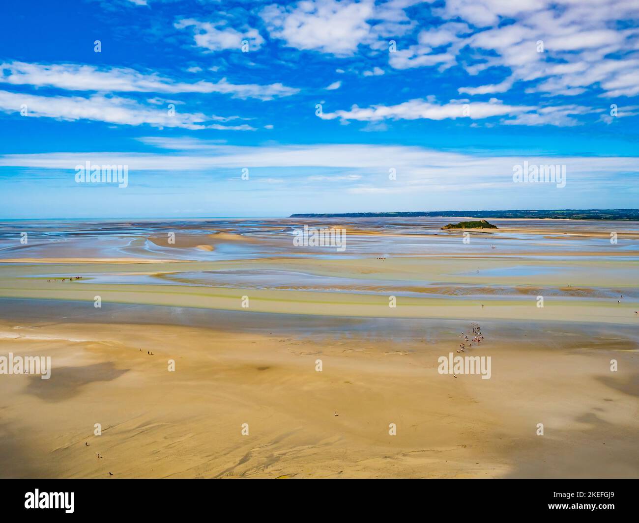 Groups of tourists walking on the colourful sand flats surrounding Le Mont Saint Michel during low tide, Normandy, Northern France Stock Photo