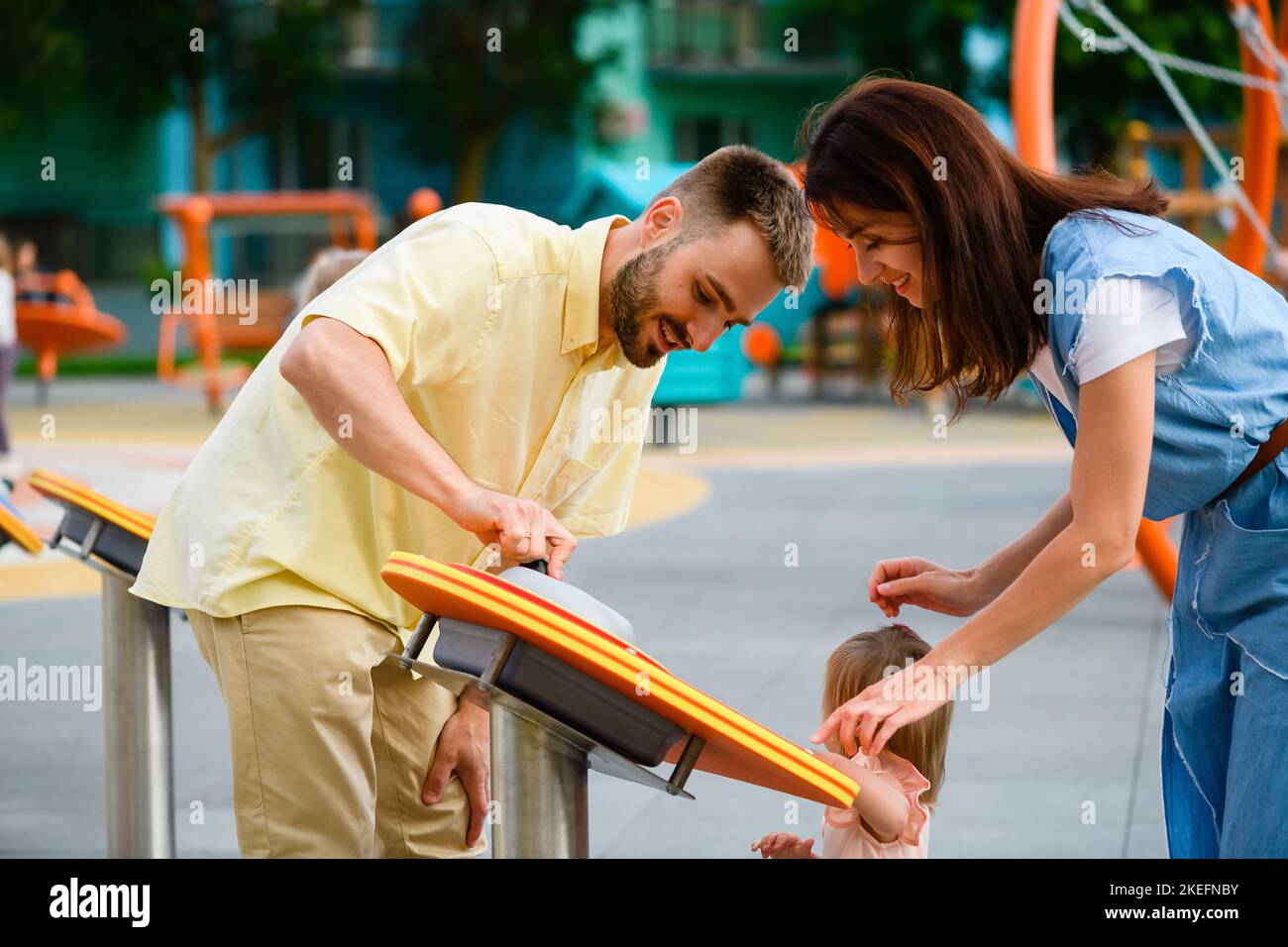 Parents and toddler girl play interactive game at playground outdoors, happy famoy time and fun together Stock Photo