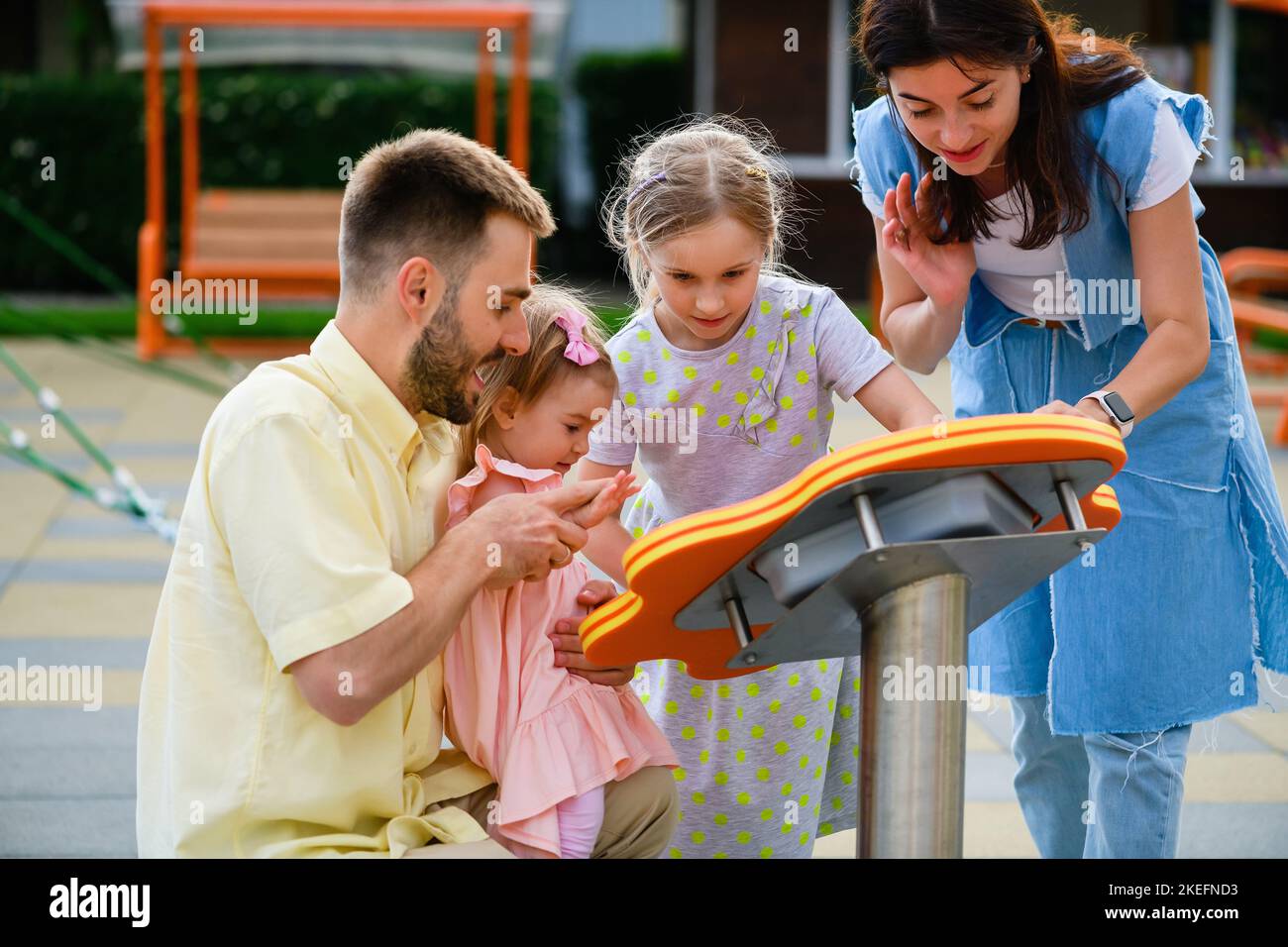 Happy young family with two female kids plaing at interactive game at modern playground, lovely people outdoors Stock Photo