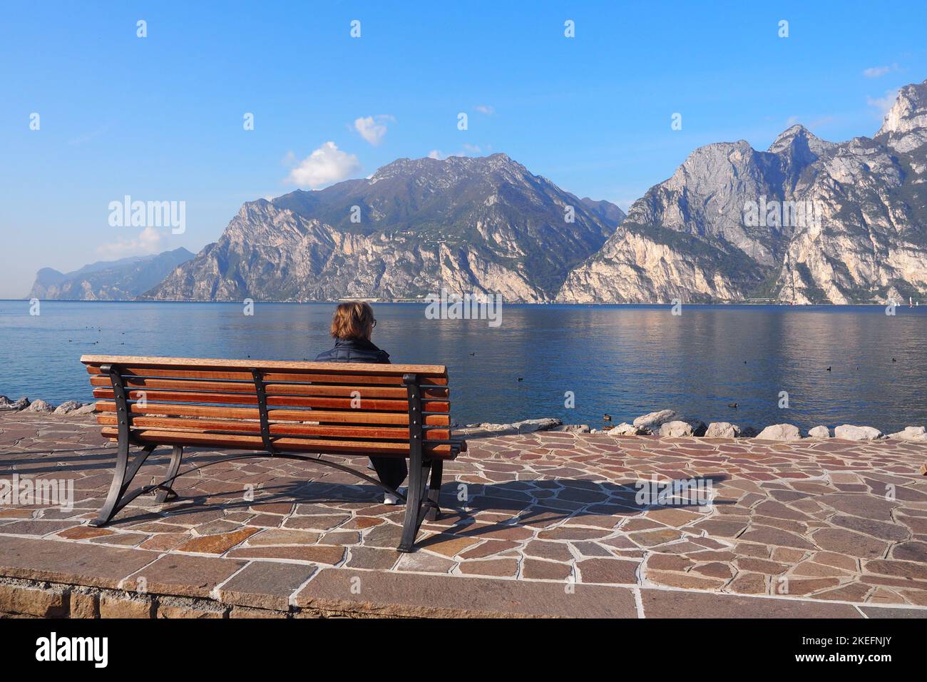 Lady sitting on a bench contemplating panorama of Lake Garda Stock Photo