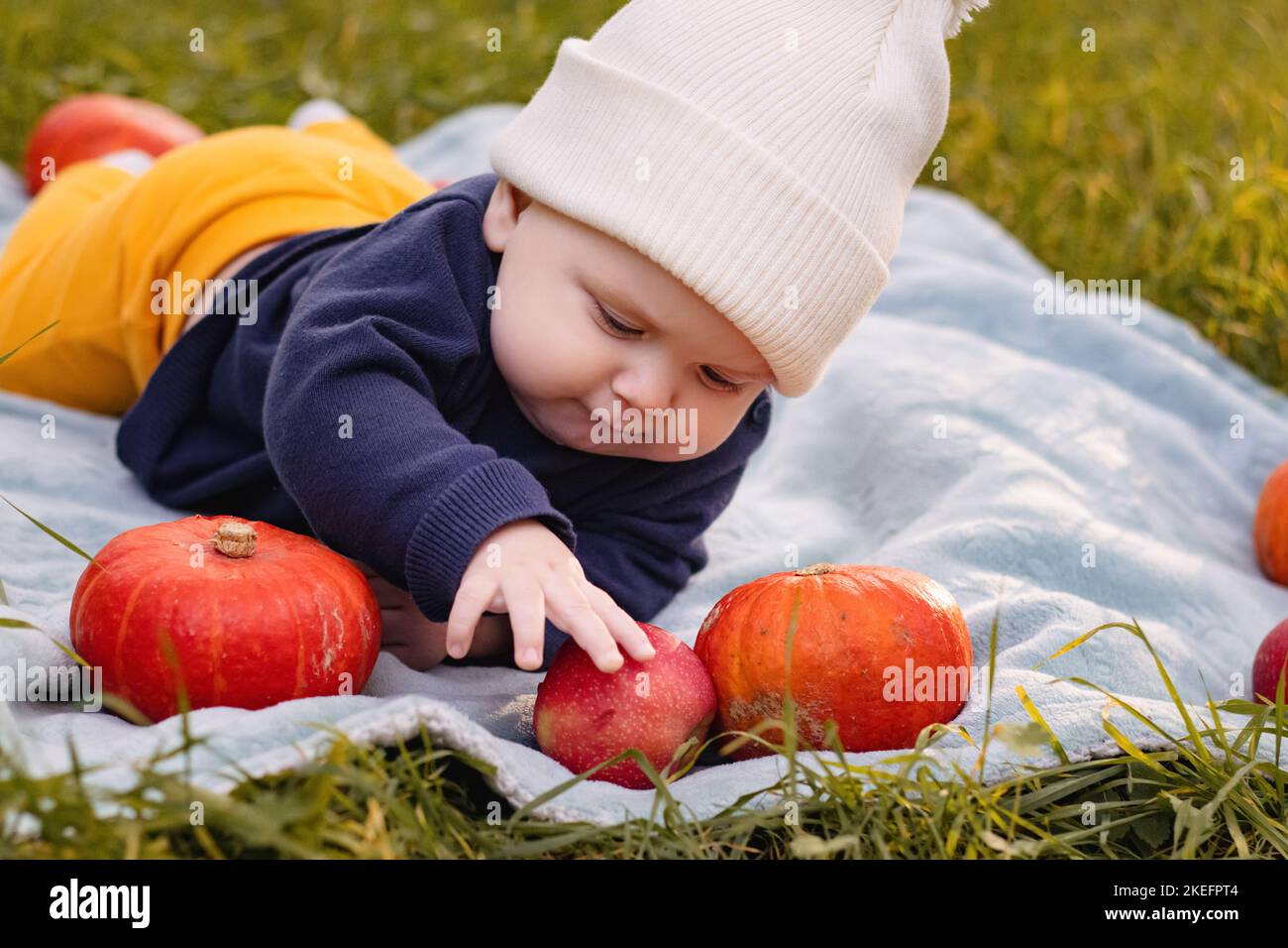 A cute little baby boy in puff ball hat is sitting on the ground in the