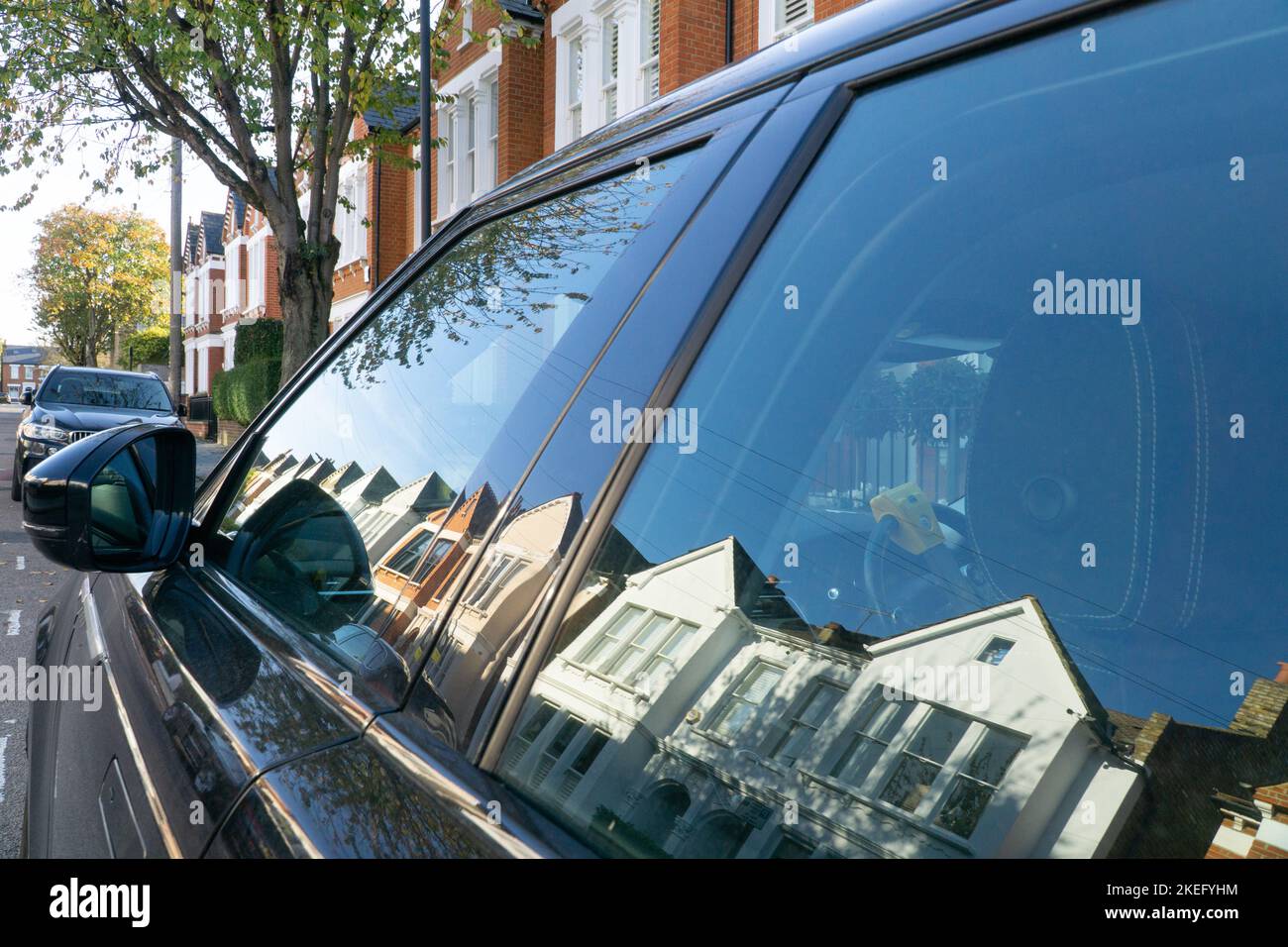 London, UK, 12 November 2022: On Hambalt Road in the Abbeville village area of Clapham a row of terraced houses in bright sunshine is reflected in the window of an SUV car. Clapham house prices are high and many luxury cars are parked on the streets. Anna Watson/Alamy Live News Stock Photo