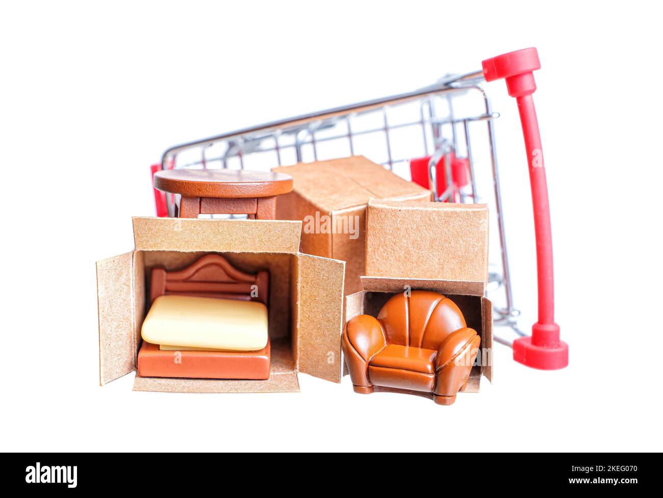 Miniature delivery boxes with tiny furniture figurines in a small shopping trolley isolated on white background. Furniture store advertising banner. Stock Photo