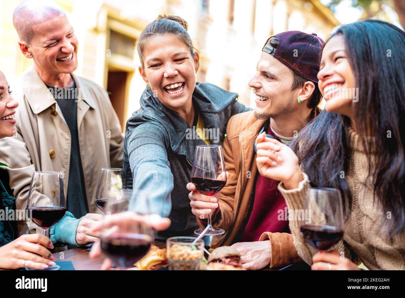 Happy friends having fun drinking red wine out side at city winery bar - Young people sharing winter time together at open air restaurant garden Stock Photo