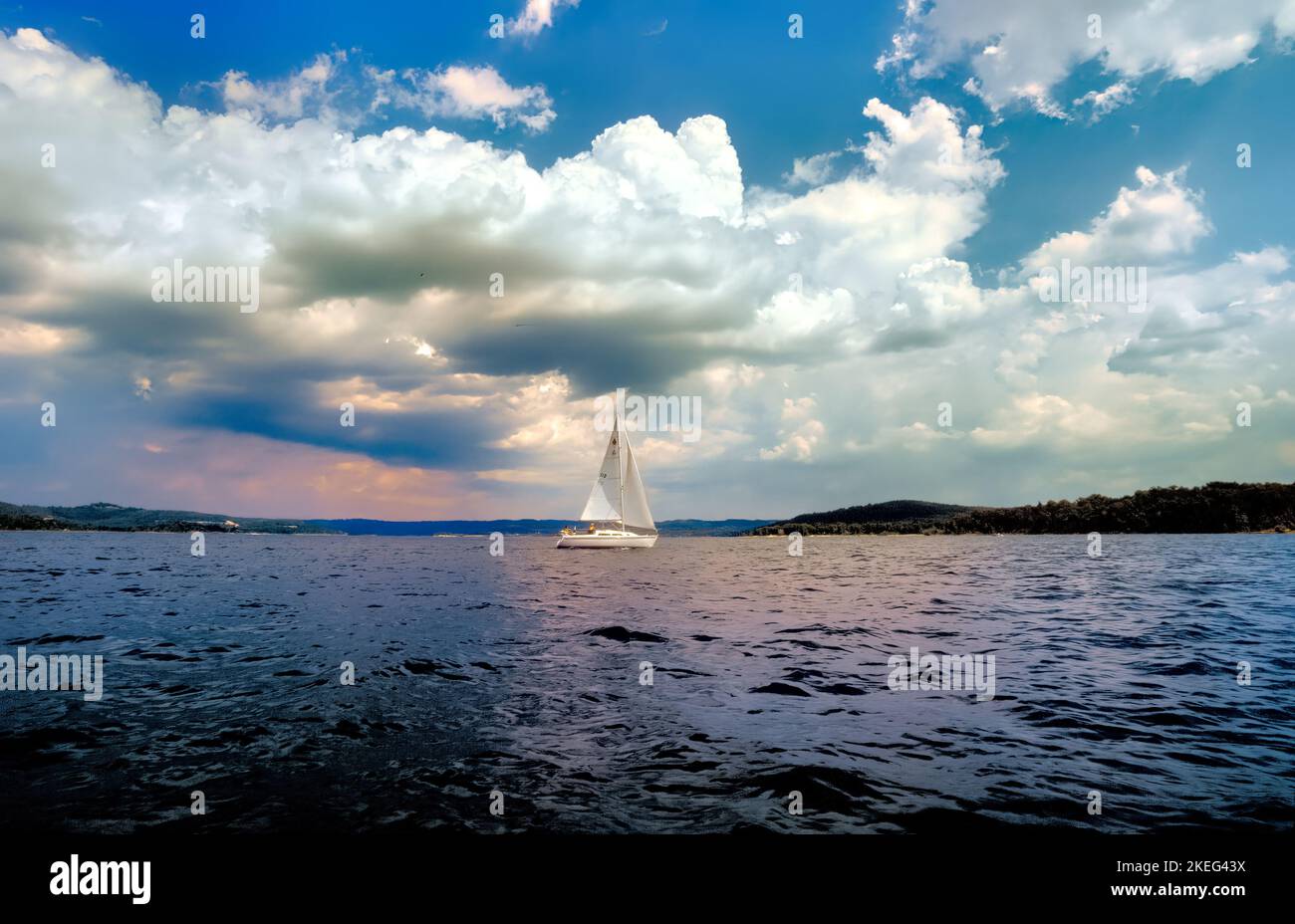 A sailboat glides across Table Rock Lake in Southern Missouri under puffy white clouds. Stock Photo