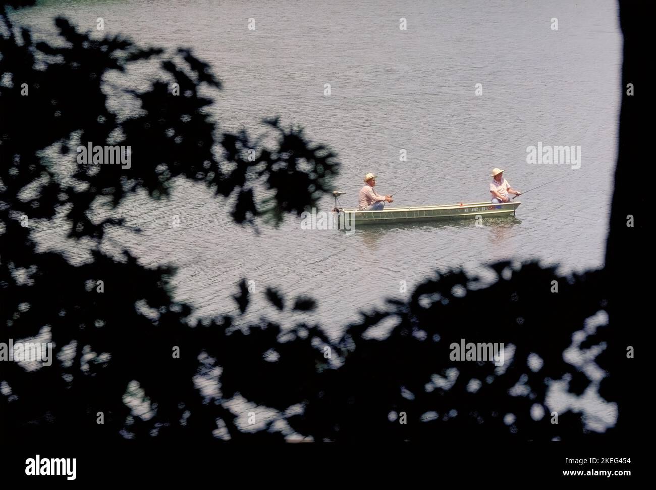 A couple fishes from a boat on Noblett Lake in the Ozarks framed by tree branches. Stock Photo