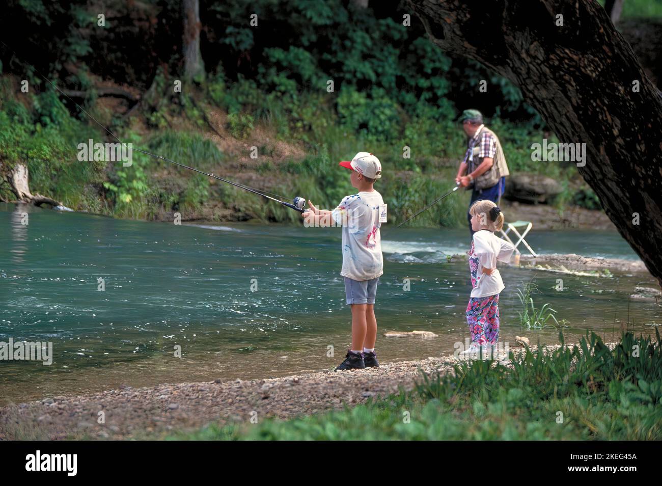 A little girl watches her big brother fish while their grandfather casts in the background at Roaring River State Park in Missouri. Stock Photo