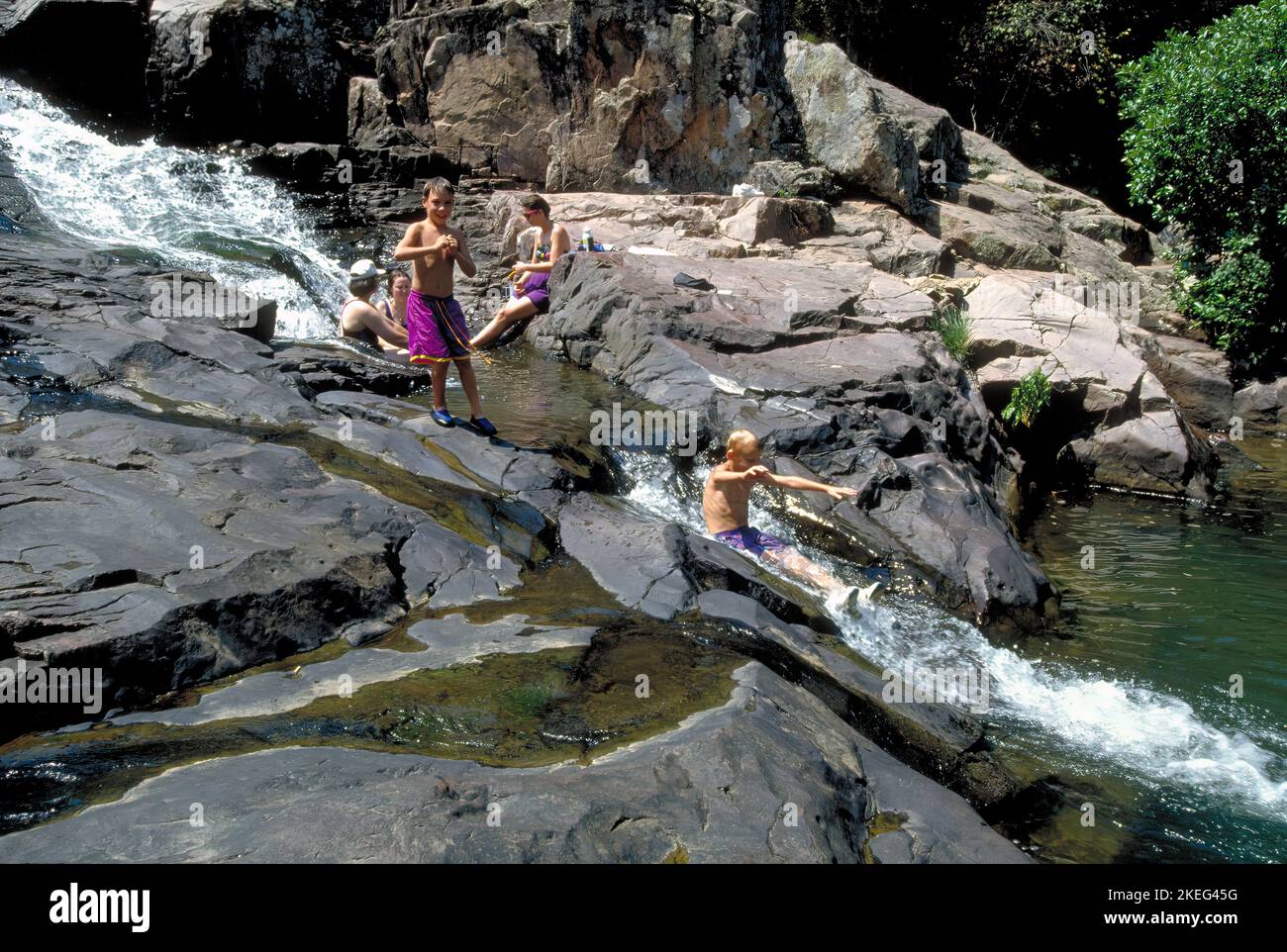 Friends escape summer heat by cooling off at Rocky Falls in eastern Missouri Ozarks. Two boys enjoy a natural waterslide created by a natural flow of Stock Photo