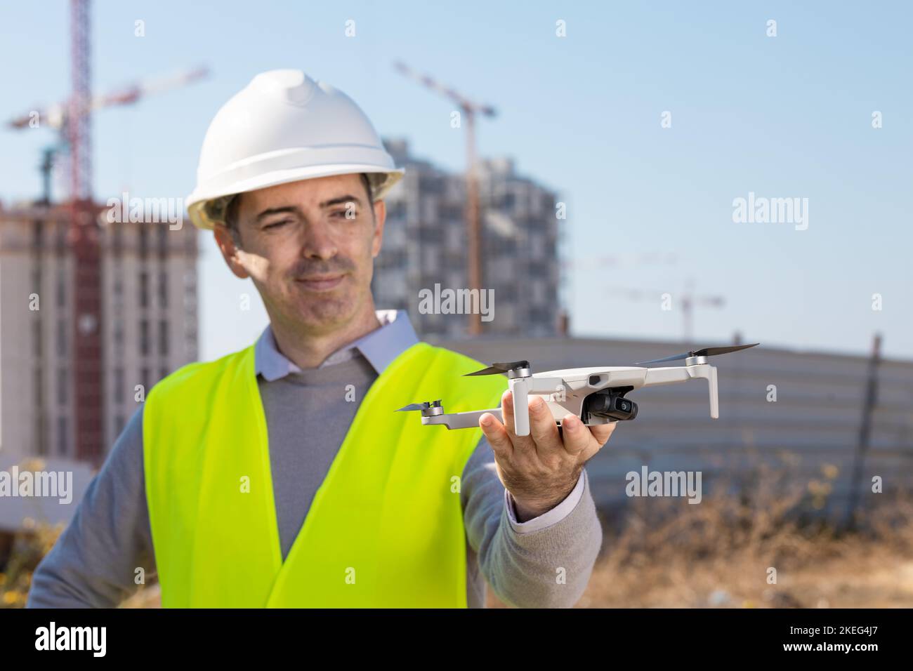 Man launches a quadcopter. An engineer flies a drone next to a construction site. Concept - construction observation with a drone.  Construction crane Stock Photo
